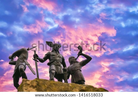 Old Norse God Odin standing on a hard rock with two Vikings, one of them is trumpeting with horn and the other raised a sword (toy plastic soldiers), burning cloudy sky, Valhalla and Ragnarok themes 