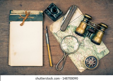 Old notebook, compass, map, vintage binoculars, pen and inkwell, pocket knife, magnifying glass on wooden background - Powered by Shutterstock