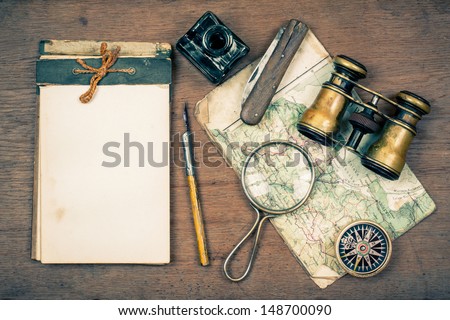 Old notebook, compass, map, vintage binoculars, pen and inkwell, pocket knife, magnifying glass on wooden background