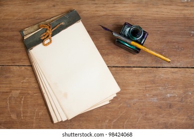 Old Notepad, Ink Pen And Inkwell On Wood Background