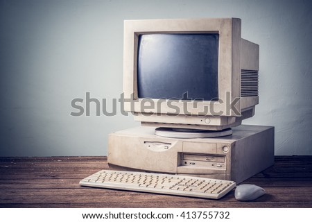 old and obsolete computer on old wood table with concrete wall background, vintage color tone