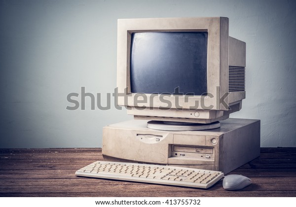 old and obsolete computer\
on old wood table with concrete wall background, vintage color\
tone