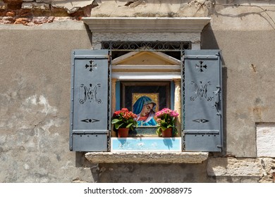 Old Open Window With Mosaic Of Virgen Mary With Flower Pot And Historic Iron Shutter