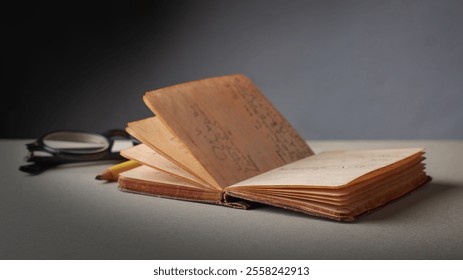 old opened hardback pocket sized diary or journal with glasses and pencil on table top, yellowed pages small brown spots and frayed edges, taken with dramatic lighting with copy space