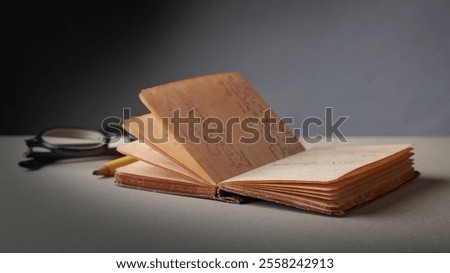 old opened hardback pocket sized diary or journal with glasses and pencil on table top, yellowed pages small brown spots and frayed edges, taken with dramatic lighting with copy space