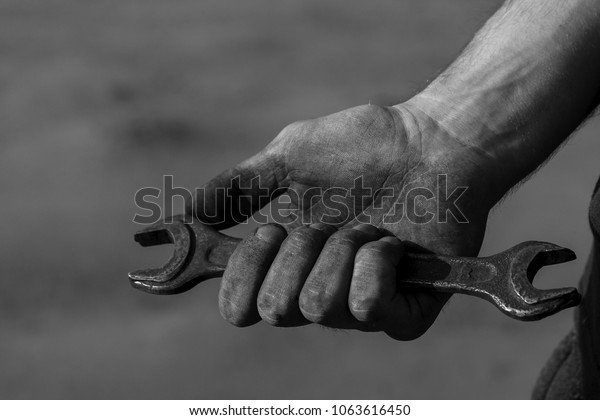 An old open-ended wrench in the hand. Working\
hands in mud, soot, dust, oil. An experienced car service master.\
Can be used as a background for an inscription, cover or part of a\
design.