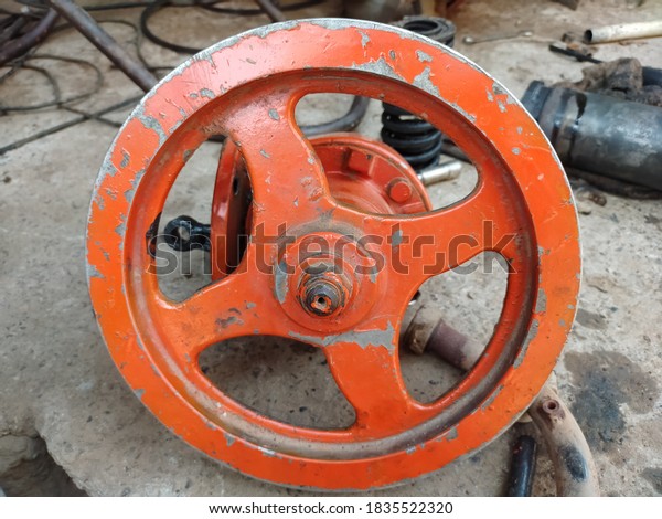 Old orange color metal pulley. old wheel for belt\
drive isolated on ground.