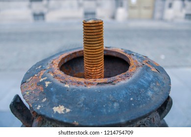 Old Orange And Rusty Metal Bolt Coming Out Of An Old Broken Streetlight With An Empty Blurry Street In The Background.