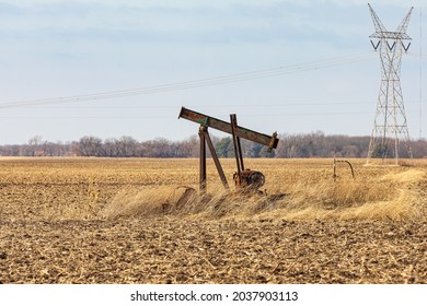 Old, Orphaned Oil Well Pump In Farm Field.  Oil Well Abandonment, Decommission, And Oil Production Concept.