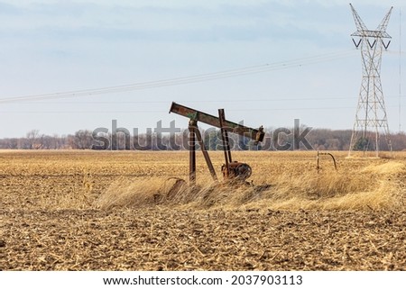 Old, orphaned oil well pump in farm field.  oil well abandonment, decommission, and oil production concept.