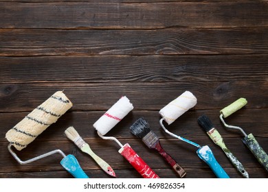 Old Paint Brushes And Rollers. Different Sizes. Top View On A Dark Wooden Background.  With Blank Place For Text. Building. Repairs.