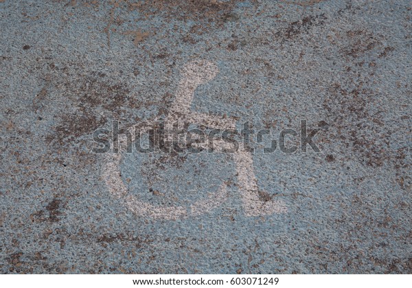 Old painted logo on the floor of a parking space\
reserved for the disabled