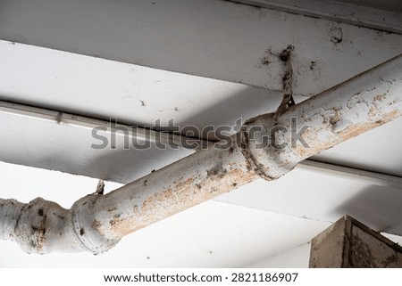 Old painted rusty drainage pipe under ceiling with peeling paint close up