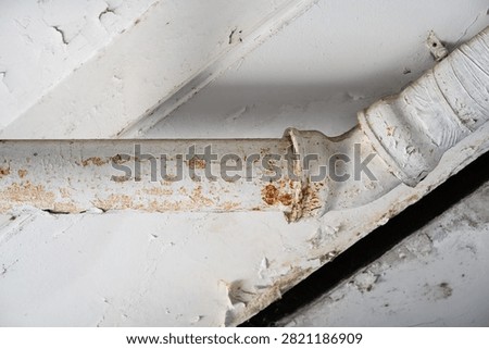 Old painted rusty drainage pipe under ceiling with peeling paint close up