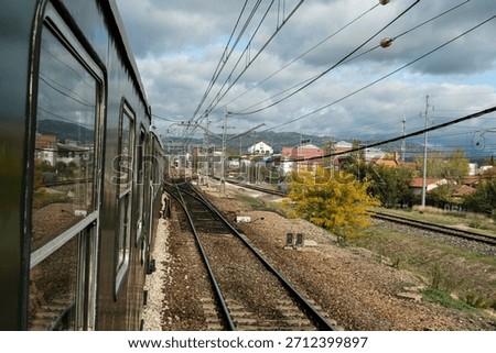 Old passenger train approaching small station with mountains in the background.