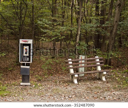 old pay phone booth and park bench in forest woods 