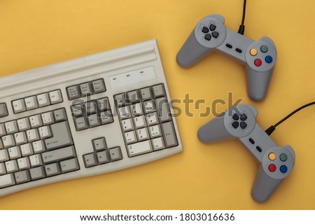 Old pc keyboard and gamepads on yellow background. Retro gaming. Video game, 80s. Top view. Flat lay