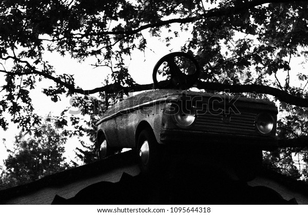 Old pedal car on the roof of children\'s playhouse,\
black and white photo