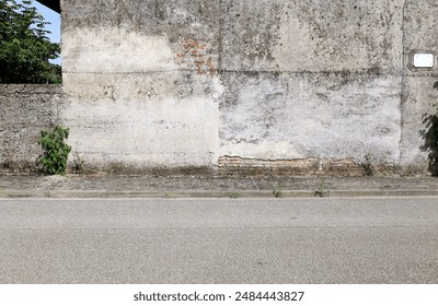 Old peeled plaster wall with brick exposed at the roadside. Weathered concrete sidewalk and street in front. Grunge background for copy space. - Powered by Shutterstock