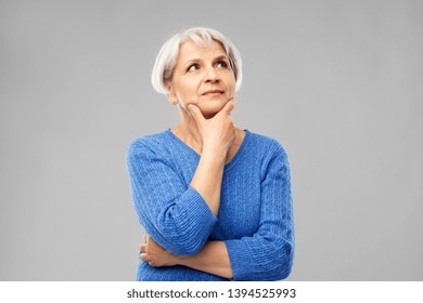 old people and decision making concept - portrait of senior woman in blue sweater thinking over grey background