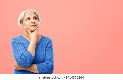 Old People And Decision Making Concept - Portrait Of Senior Woman In Blue Sweater Thinking Over Pink Or Living Coral Background