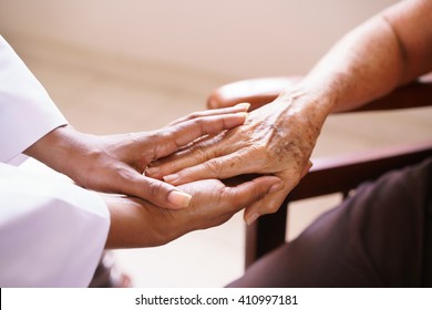 Old people in geriatric hospice: Aged patient receives the visit of a female black doctor. They shake their hands and talk in the hospital.