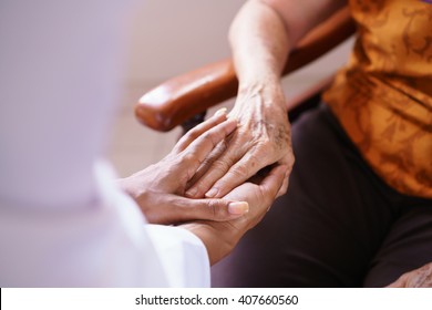 Old people in geriatric hospice: Black doctor visiting an aged patient, holding hands of a senior woman. Concept of comfort and compassion