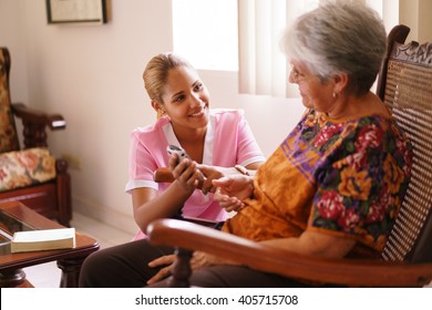 Old people in geriatric hospice: elderly lady having eyesight problems viewing the screen of mobile phone. A nurse helps the senior woman dialing a number on the tiny keyboard 