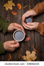 Old people hands. Closeup. The senior people hand holding a cup of coffee on the wood table covered with autumn leaves. Old age concept.