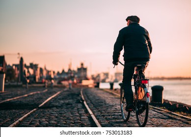 Old Person Riding A Bicycle In Antwerp, Belgium During Sunset.