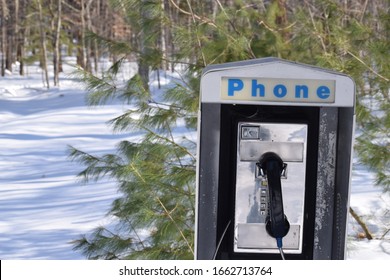 Old phone booth in a park, surrounded by trees. Public payphone in the forest. Remote communication. Campground telephone in nature during the winter, with snow in the background