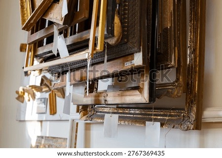 Old picture frames are stacked in a storage area. The collection shows different styles and sizes, waiting for new artwork.