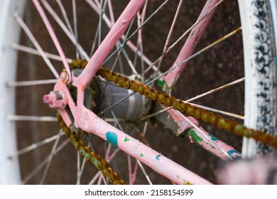 An old pink bicycle, forgotten on the street. An old ring with a rusty chain from a pink bicycle parked on the street. Rusty bicycle rear wheel, including chain and rear sprocket selective focus.
