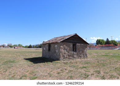 An Old Pioneer Cabin Made Of Stone In Central Utah, With A Stadium In The Background