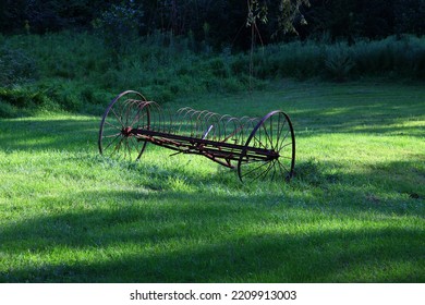 An Old Plough In A Green Meadow Lit By Dappled Sunlight.