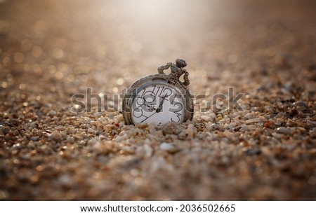 An old pocket watch dropped on the sand, in warm light and bokeh background - thinking and controlling the concept of time.