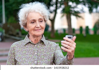 An Old Pretty Blond Woman Takes A Selfie In A City Park. Women Over 60 Years