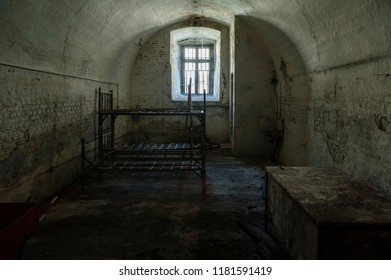 Old Prison Cell/abandoned Prison Cell With Metal Bunk Beds And Sitting Platform And Steel Bars At The Small Window.