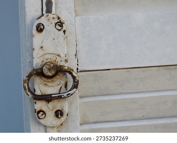 Old pull ring and lock of a white wooden shutters on light blue textured wall. Old white shutters closeup.	