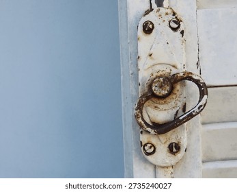 Old pull ring and lock of a white wooden shutters on light blue textured wall. Old white shutters closeup.