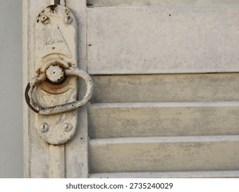 Old pull ring and lock of a white wooden shutters on light blue textured wall. Old white shutters closeup.
