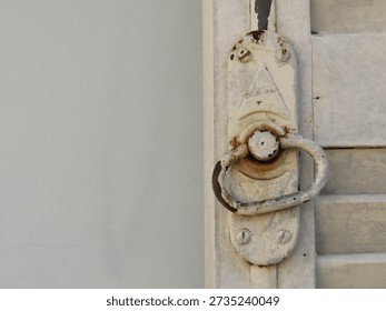 Old pull ring and lock of a white wooden shutters on light blue textured wall. Old white shutters closeup.
