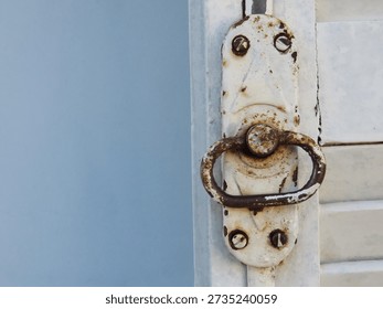 Old pull ring and lock of a white wooden shutters on light blue textured wall. Old white shutters closeup.