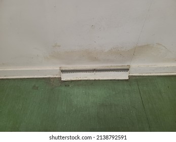 An old radiator at the base of a dirty wall. The wall is discolored and yellowing around the old heating system.