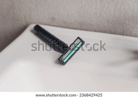 An old razor with a rusty blade that has been used before placed on the edge of the basin in the bathroom.
