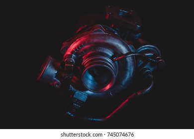 An old reconditioned car turbine, turbocharger, isolated on black with dramatic red and blue lighting.