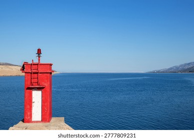 Old rectangular bright red lighthouse on the cliff at the coast of Adriatic sea, Croatia in front of the  blue sea and a clear sky  on a beautiful sunny day
