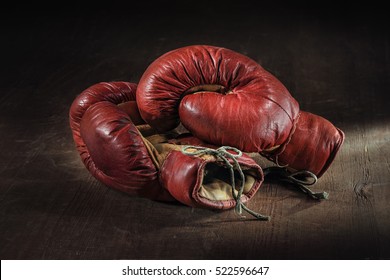 Old red boxing gloves on wooden background.