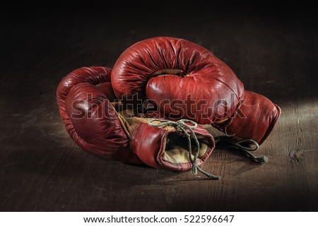 Old red boxing gloves on wooden background.