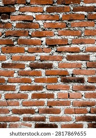 Old red brick wall with rough cement mortar, showcasing weathered textures and rustic masonry. Ideal as a construction, architecture, or background pattern
